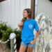Woman in blue shirt by surfboard outdoors.