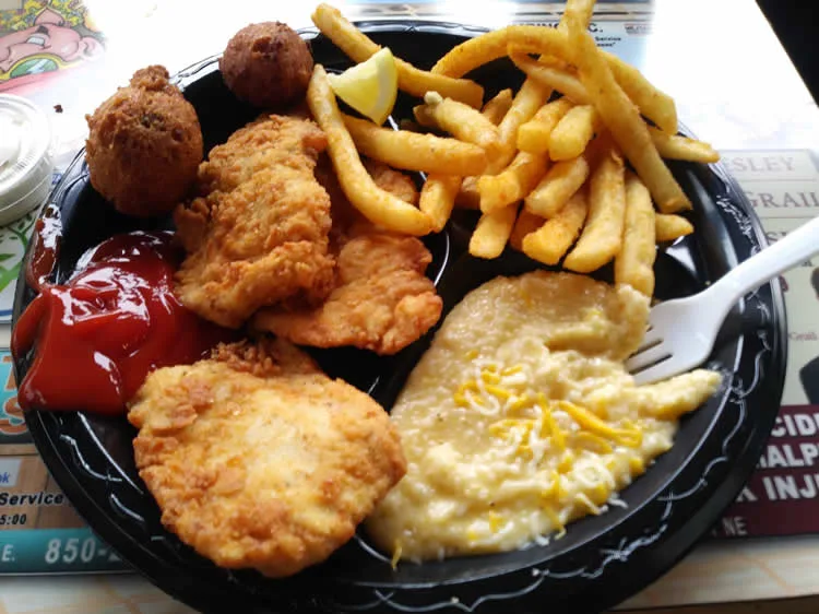 Fried fish, french fries, hush puppies, grits on plate.