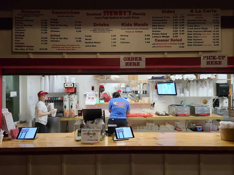 Restaurant counter with menu and staff serving orders.