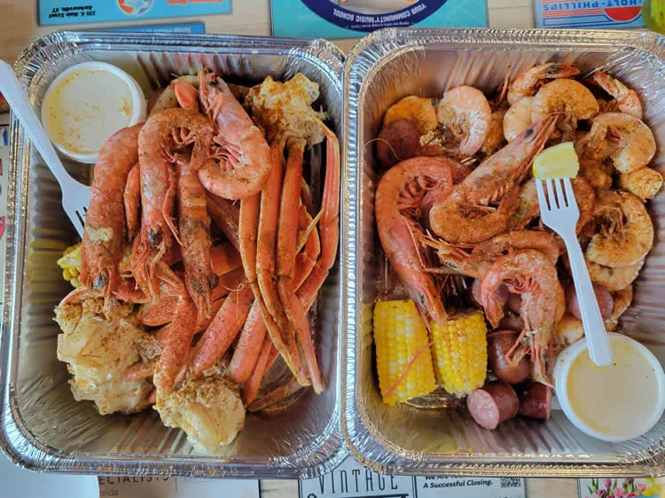 Two trays of seafood boil with shrimp, crab, corn.