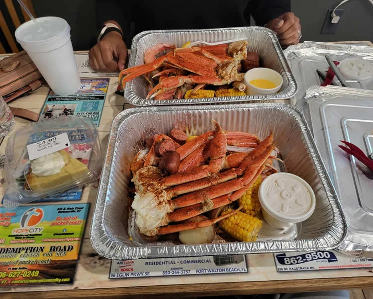 Seafood boil with crab, corn, and potatoes in trays.